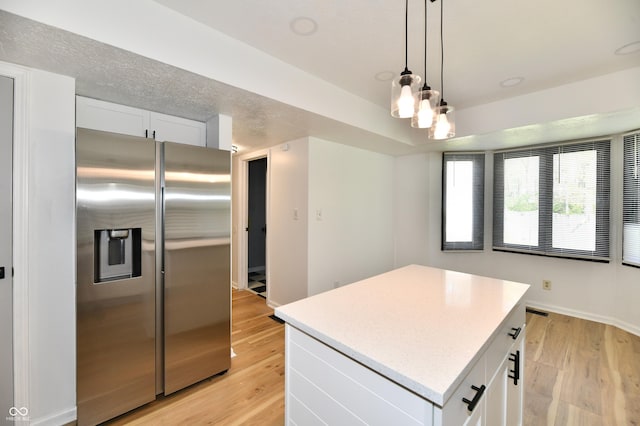 kitchen with stainless steel fridge, light wood finished floors, a center island, white cabinetry, and decorative light fixtures