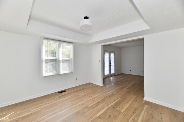 empty room with plenty of natural light, light wood finished floors, a tray ceiling, and visible vents