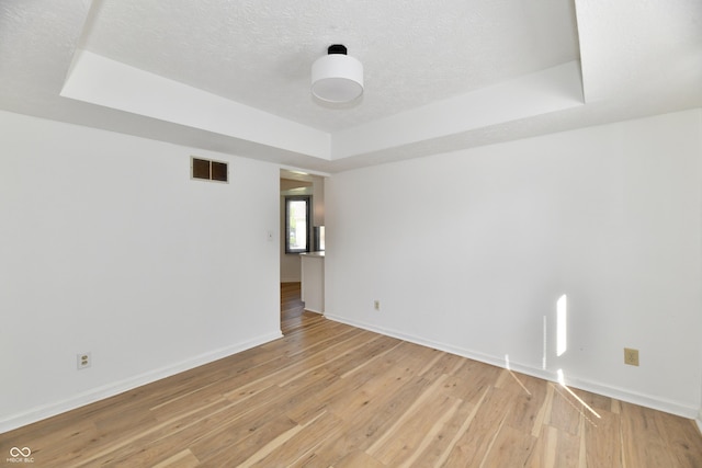 unfurnished room featuring a raised ceiling, baseboards, light wood-style flooring, and visible vents