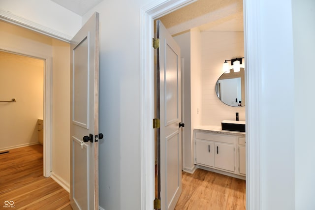 hallway with a sink, baseboards, light wood finished floors, and visible vents