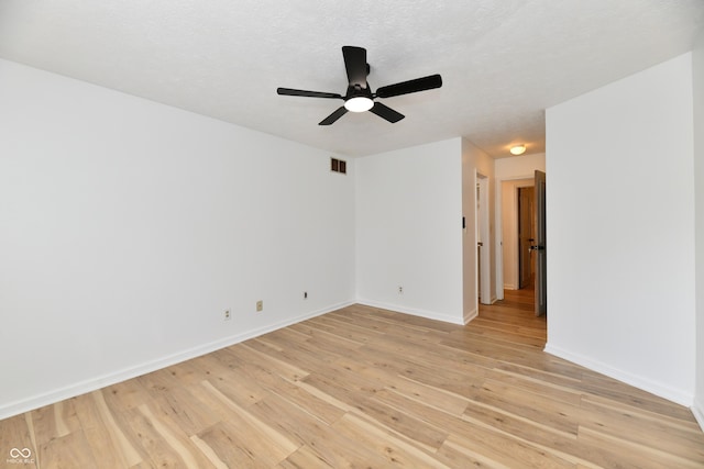 empty room with baseboards, a ceiling fan, light wood finished floors, and visible vents