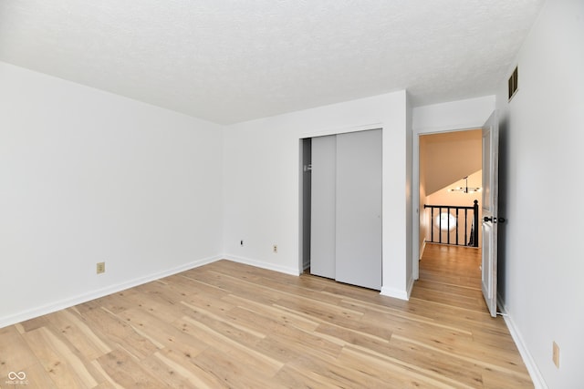 unfurnished bedroom featuring a textured ceiling, baseboards, visible vents, and light wood-style floors