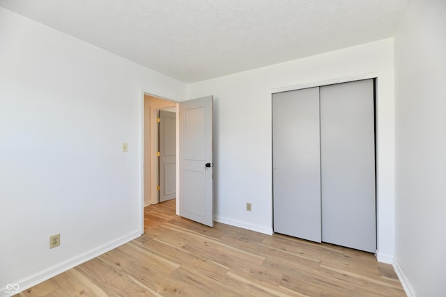 unfurnished bedroom featuring baseboards, light wood finished floors, and a closet