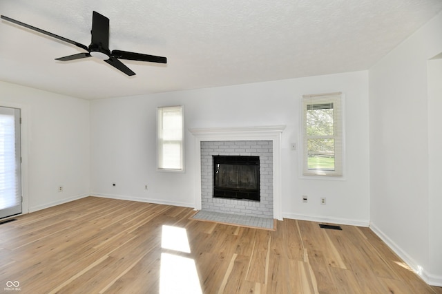 unfurnished living room featuring visible vents, a brick fireplace, light wood finished floors, and a wealth of natural light