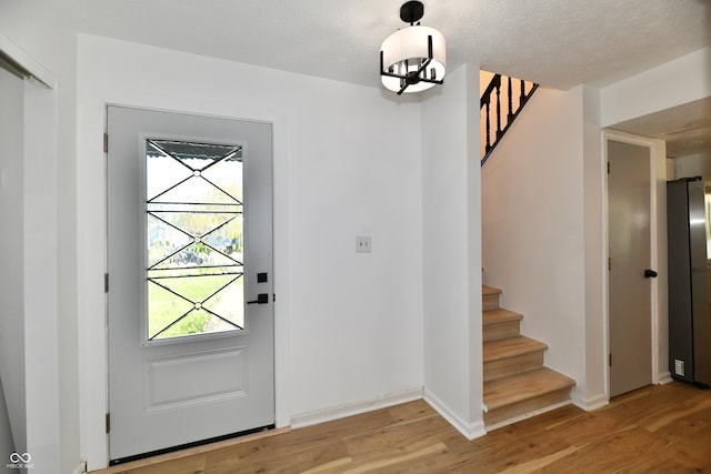 foyer entrance with baseboards, light wood finished floors, stairway, and an inviting chandelier