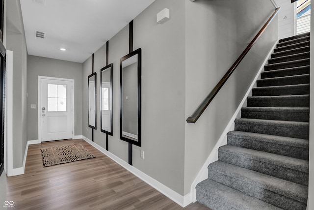 foyer entrance featuring a wealth of natural light, stairs, wood finished floors, and visible vents