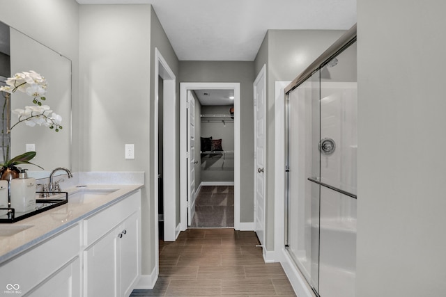 full bathroom with a sink, baseboards, a shower stall, and double vanity