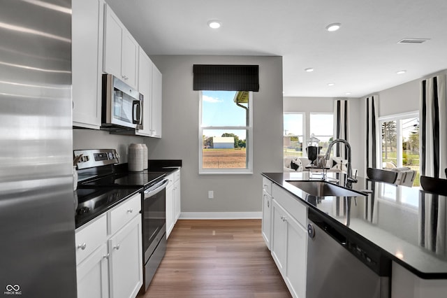 kitchen with a sink, appliances with stainless steel finishes, dark countertops, and wood finished floors