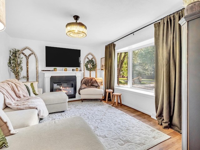 living area with a glass covered fireplace, baseboards, and light wood-type flooring