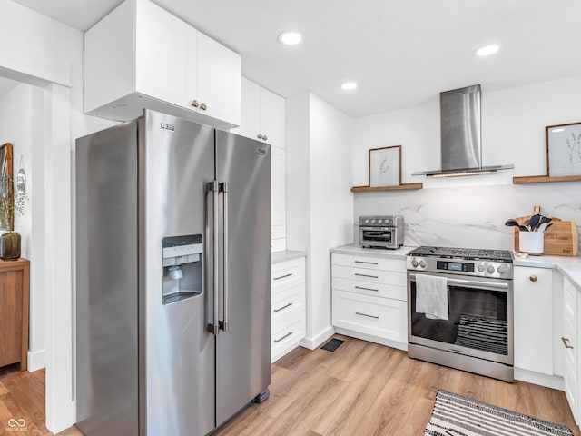 kitchen with appliances with stainless steel finishes, open shelves, light wood finished floors, and wall chimney exhaust hood