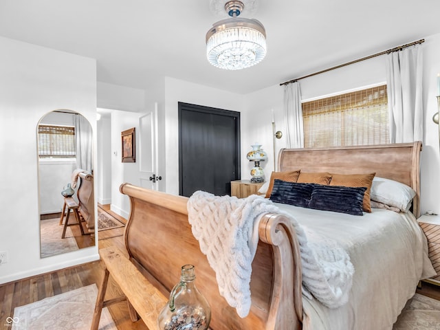 bedroom with baseboards, wood finished floors, a notable chandelier, and a closet