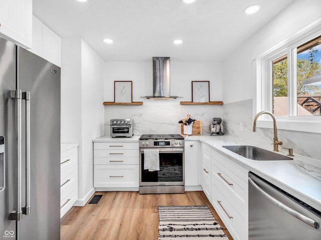 kitchen featuring wall chimney range hood, open shelves, appliances with stainless steel finishes, a sink, and light wood-type flooring