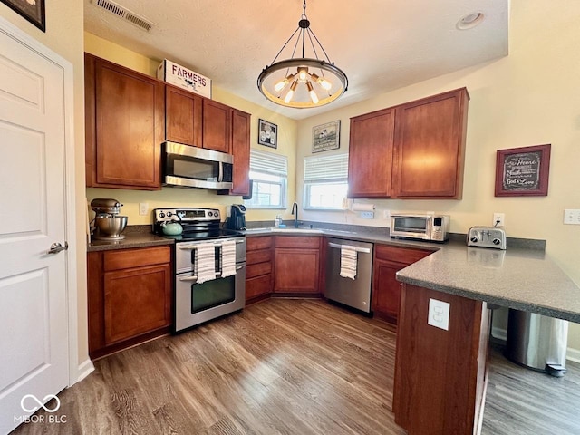 kitchen featuring dark wood-type flooring, a peninsula, visible vents, and stainless steel appliances