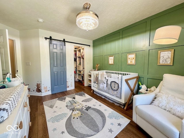bedroom featuring a barn door, a walk in closet, a chandelier, baseboards, and dark wood-style floors