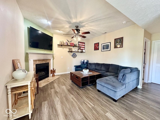 living room featuring a fireplace, a textured ceiling, a ceiling fan, baseboards, and wood finished floors