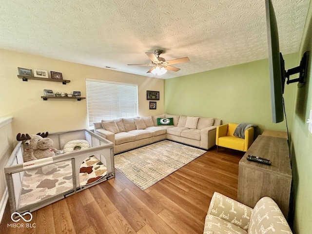 living area with a textured ceiling, ceiling fan, visible vents, and wood finished floors