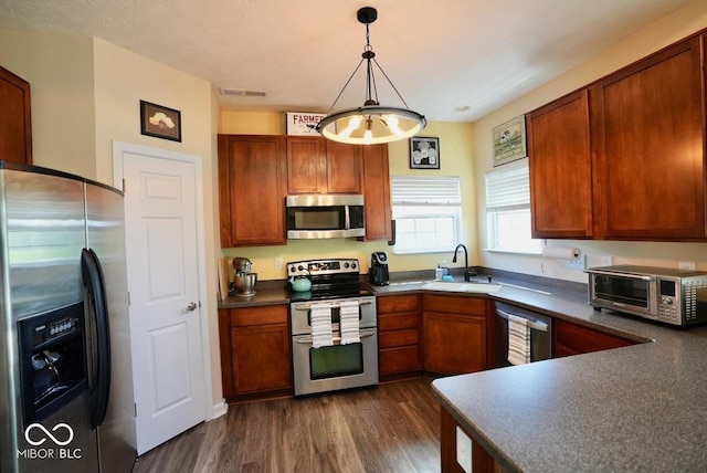 kitchen featuring a toaster, dark countertops, dark wood-style floors, a sink, and stainless steel appliances