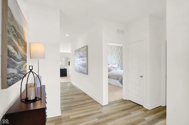 corridor featuring baseboards, visible vents, and light wood-style flooring