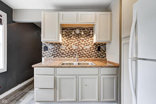 kitchen featuring white cabinets, a sink, freestanding refrigerator, decorative backsplash, and wood finished floors
