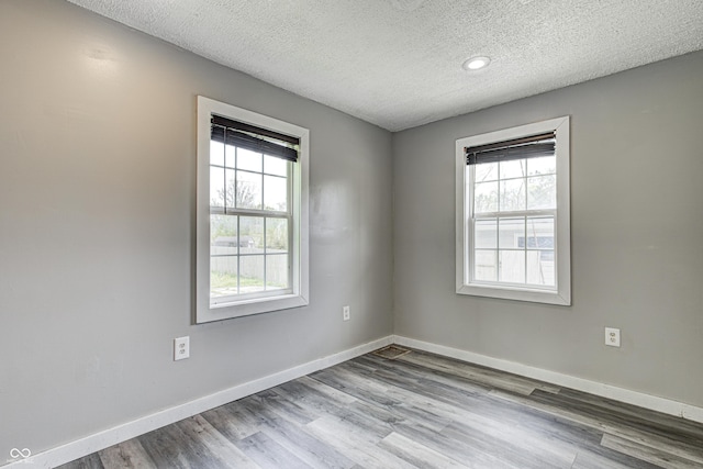 empty room with baseboards, a textured ceiling, a wealth of natural light, and wood finished floors