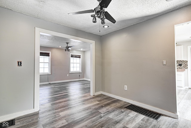 empty room with a ceiling fan, a textured ceiling, visible vents, wood finished floors, and baseboards