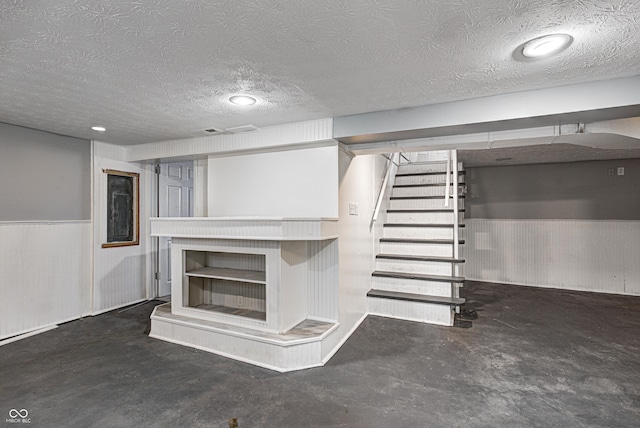 finished basement featuring a textured ceiling, a wainscoted wall, and stairway