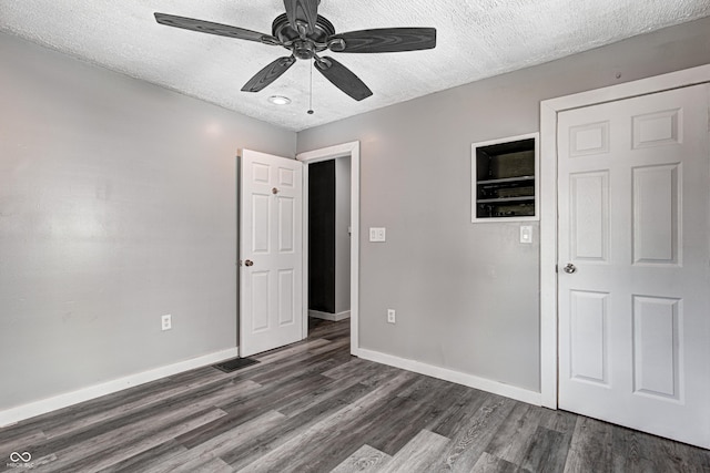 unfurnished bedroom with a ceiling fan, a textured ceiling, visible vents, baseboards, and dark wood-style floors