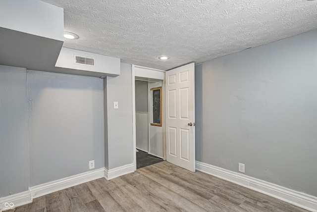 unfurnished bedroom featuring a textured ceiling, visible vents, wood finished floors, baseboards, and recessed lighting