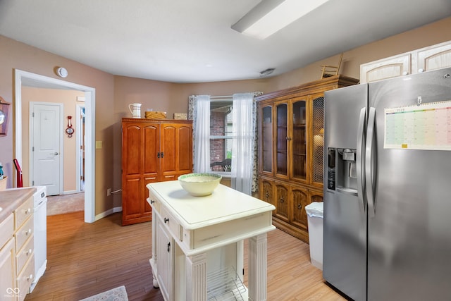 kitchen featuring baseboards, stainless steel fridge, light countertops, white cabinets, and light wood finished floors