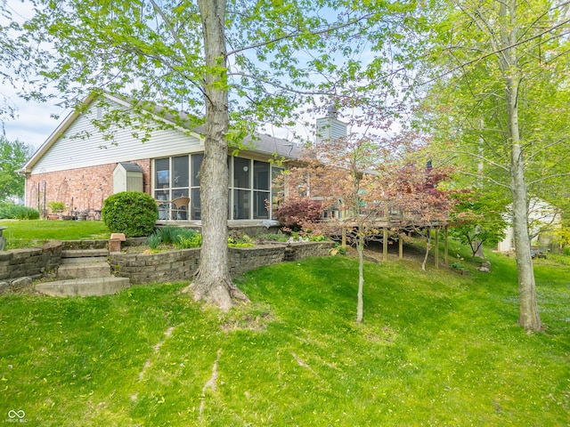 rear view of property with a lawn, a sunroom, a deck, and brick siding