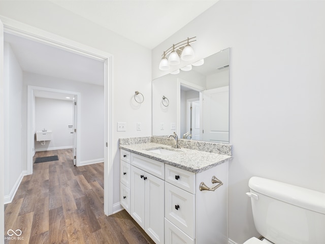 half bath featuring vanity, toilet, baseboards, wood finished floors, and visible vents
