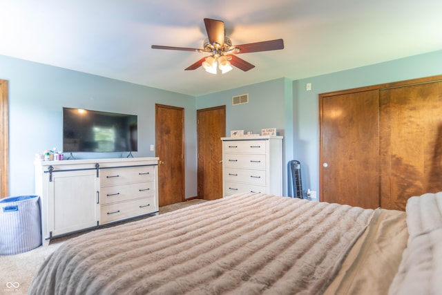 carpeted bedroom featuring visible vents, multiple closets, and ceiling fan