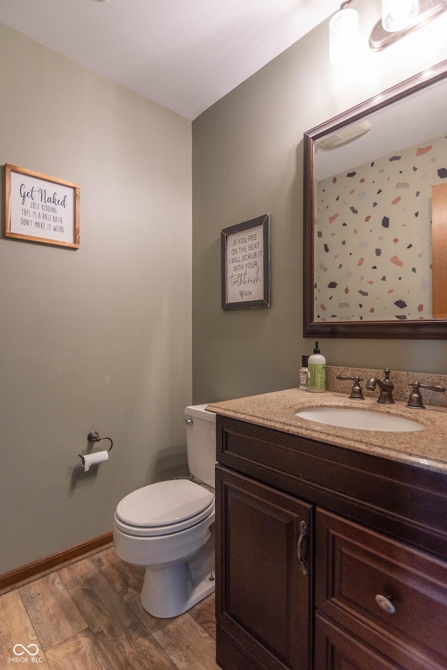 half bathroom with toilet, wood finished floors, and vanity