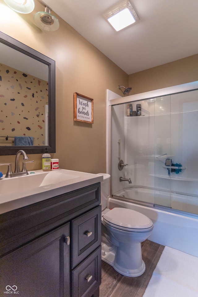 bathroom with toilet, combined bath / shower with glass door, wood finished floors, and vanity