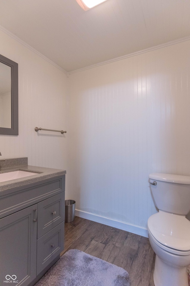 half bathroom featuring vanity, crown molding, wood finished floors, toilet, and baseboards