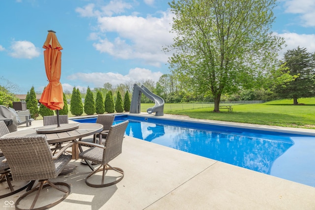 outdoor pool with a lawn, a patio area, fence, a water slide, and outdoor dining space