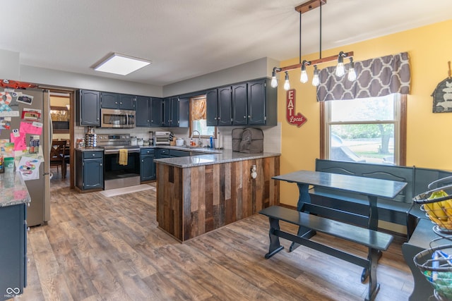 kitchen featuring appliances with stainless steel finishes, a sink, a peninsula, wood finished floors, and backsplash