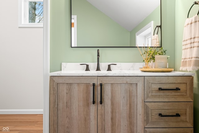 bathroom featuring baseboards, wood finished floors, lofted ceiling, and vanity