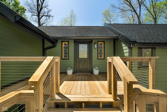 view of exterior entry with a shingled roof and a deck