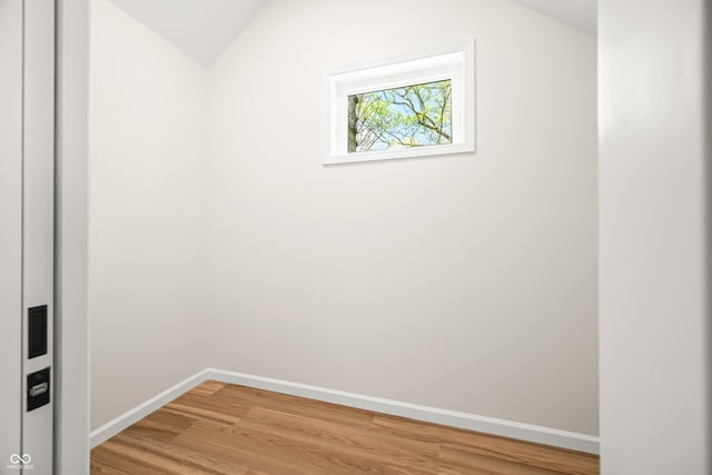 empty room with baseboards, vaulted ceiling, and light wood-type flooring