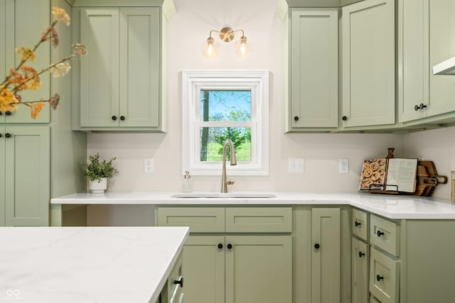 kitchen featuring green cabinetry, light stone counters, and a sink