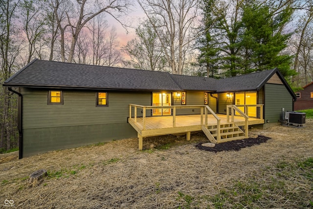 back of house at dusk featuring roof with shingles, central AC unit, and a wooden deck