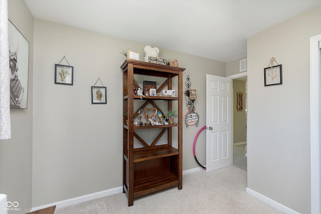 hall with baseboards, visible vents, and light carpet