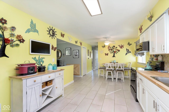 kitchen with light tile patterned floors, ceiling fan, black range with electric cooktop, and white cabinetry