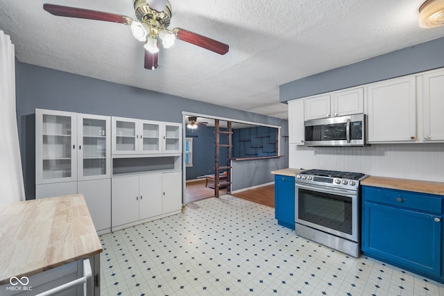 kitchen with stainless steel appliances, white cabinets, ceiling fan, butcher block counters, and blue cabinetry