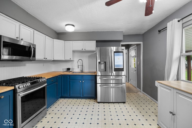 kitchen featuring butcher block countertops, a sink, blue cabinetry, white cabinets, and appliances with stainless steel finishes