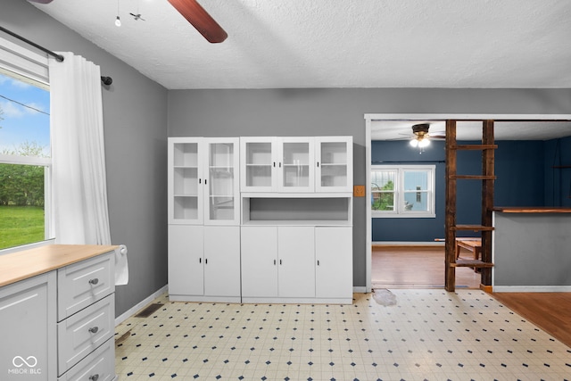 kitchen featuring light floors, a textured ceiling, white cabinetry, and a ceiling fan