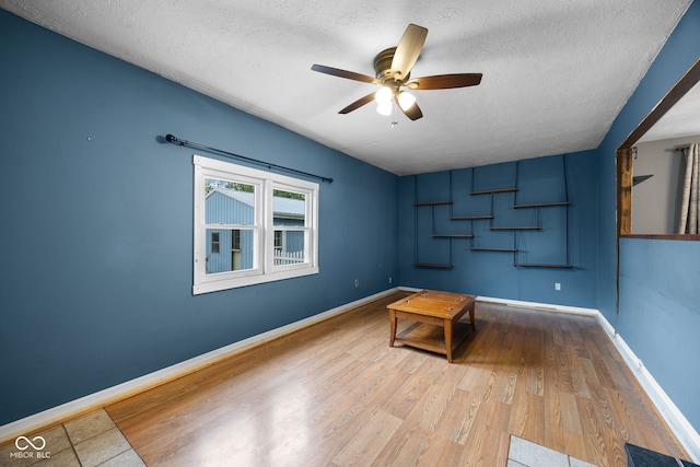 interior space with a textured ceiling, wood finished floors, baseboards, and ceiling fan