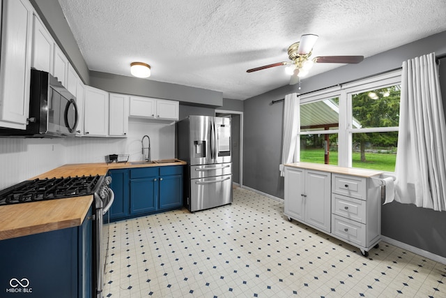 kitchen featuring a ceiling fan, wood counters, baseboards, appliances with stainless steel finishes, and blue cabinetry