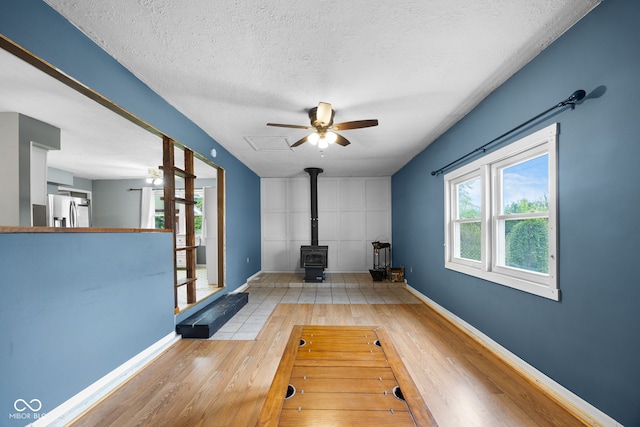 exercise room featuring wood finished floors, a wood stove, a textured ceiling, a ceiling fan, and baseboards